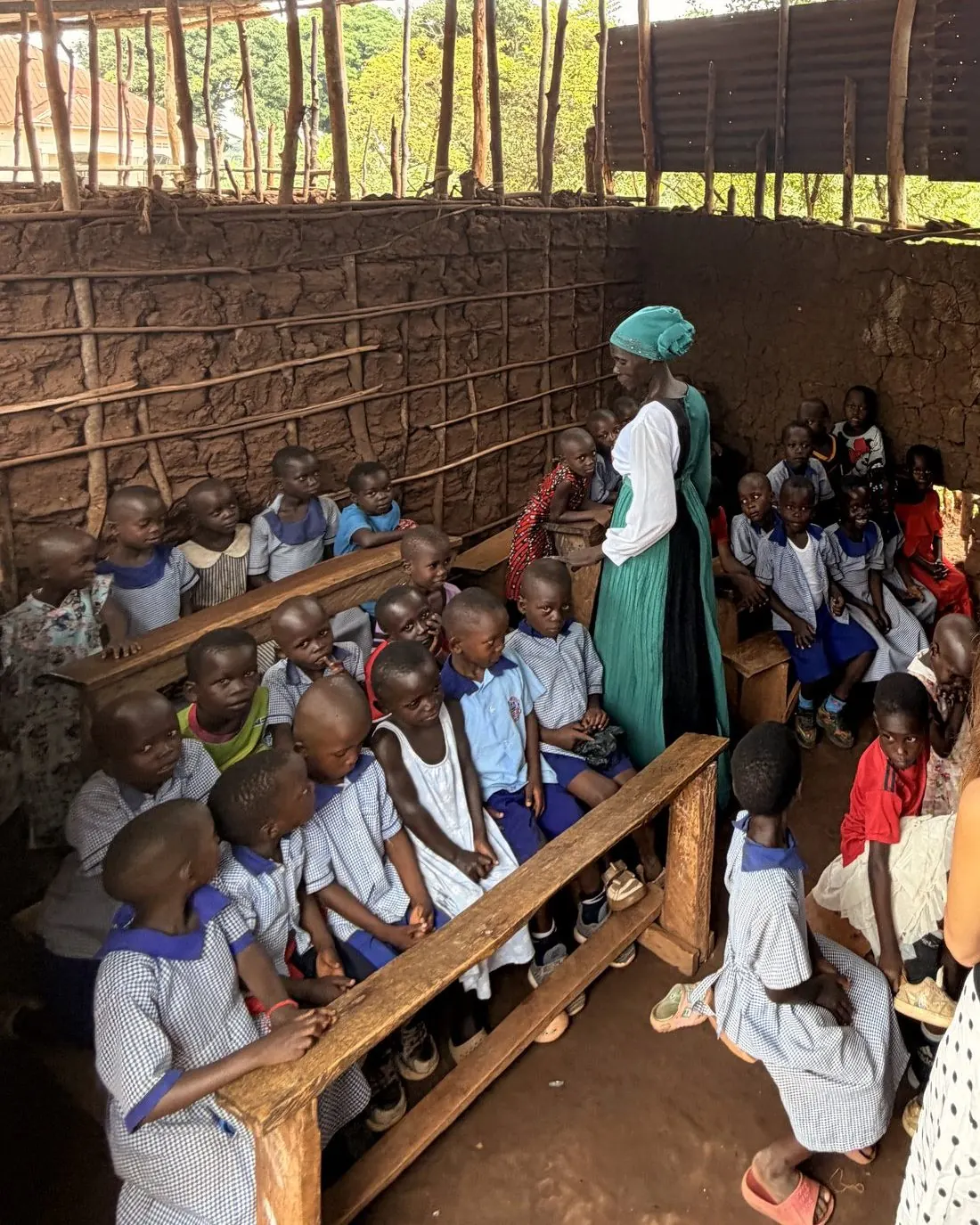 A teacher with students at wooden desks in an open-sided temporary classroom