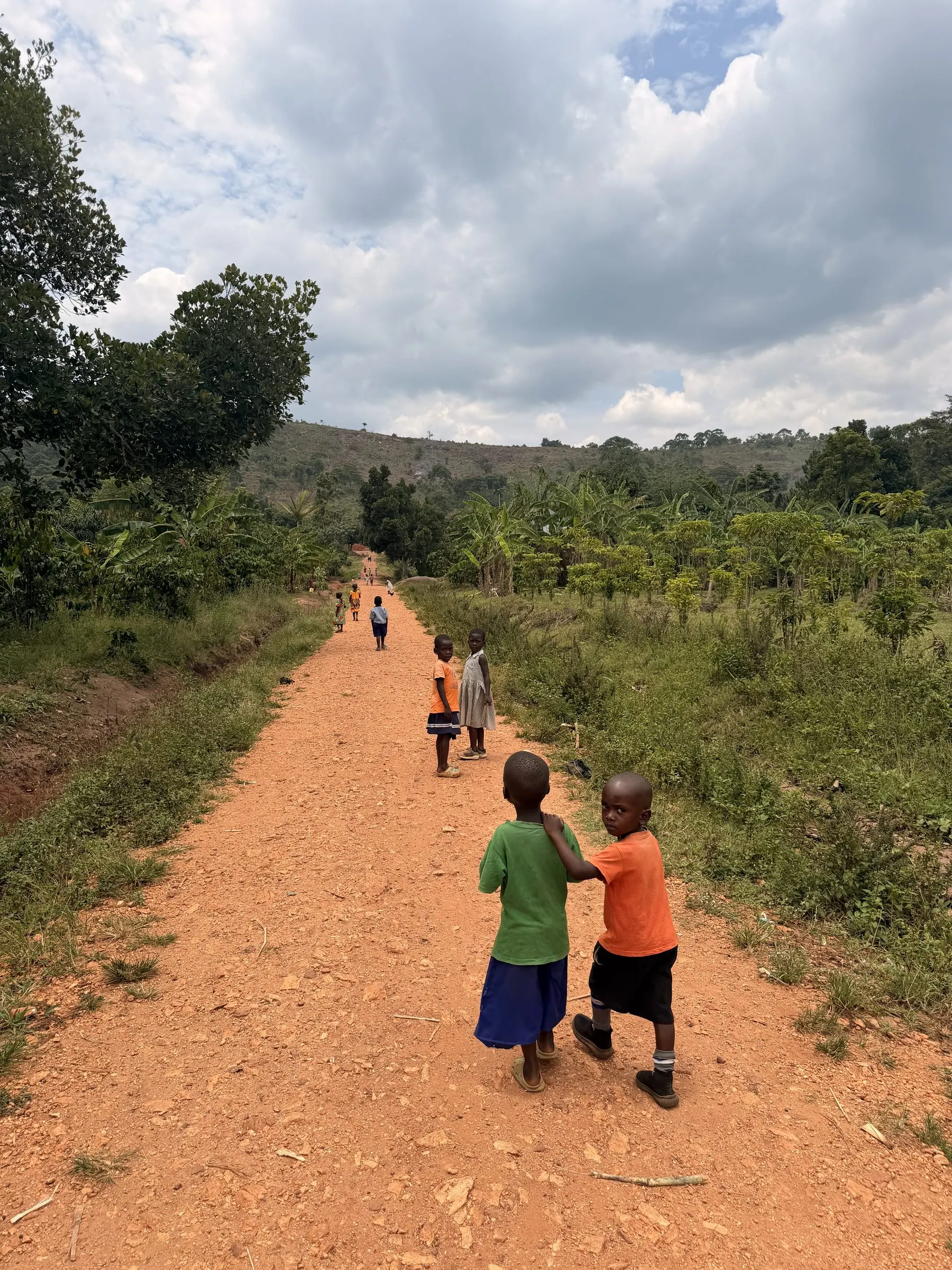 Two children walking down the red-earth road toward the school