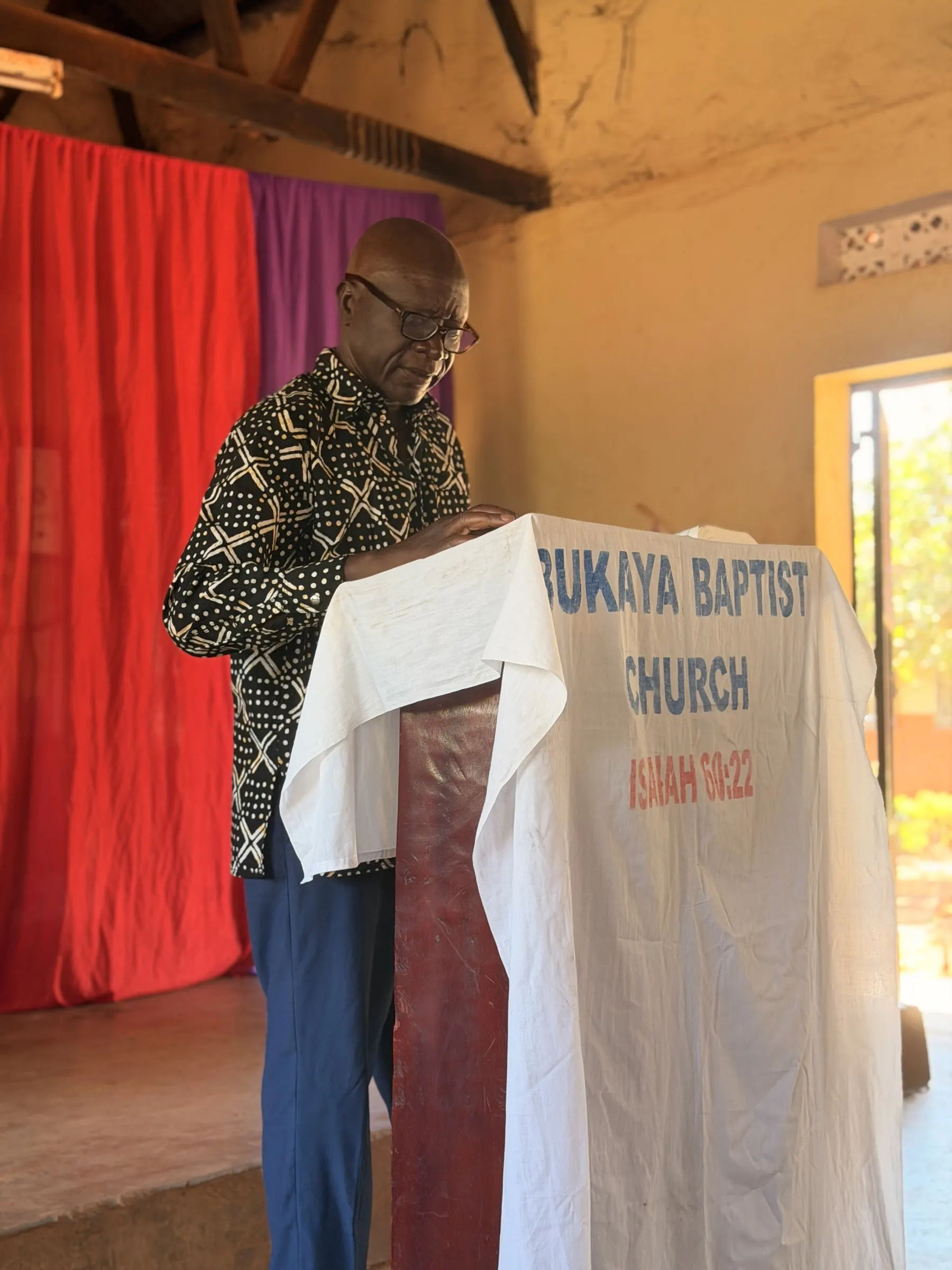 Pastor Nelson Ntanda standing at the pulpit of Bukaya Baptist Church
